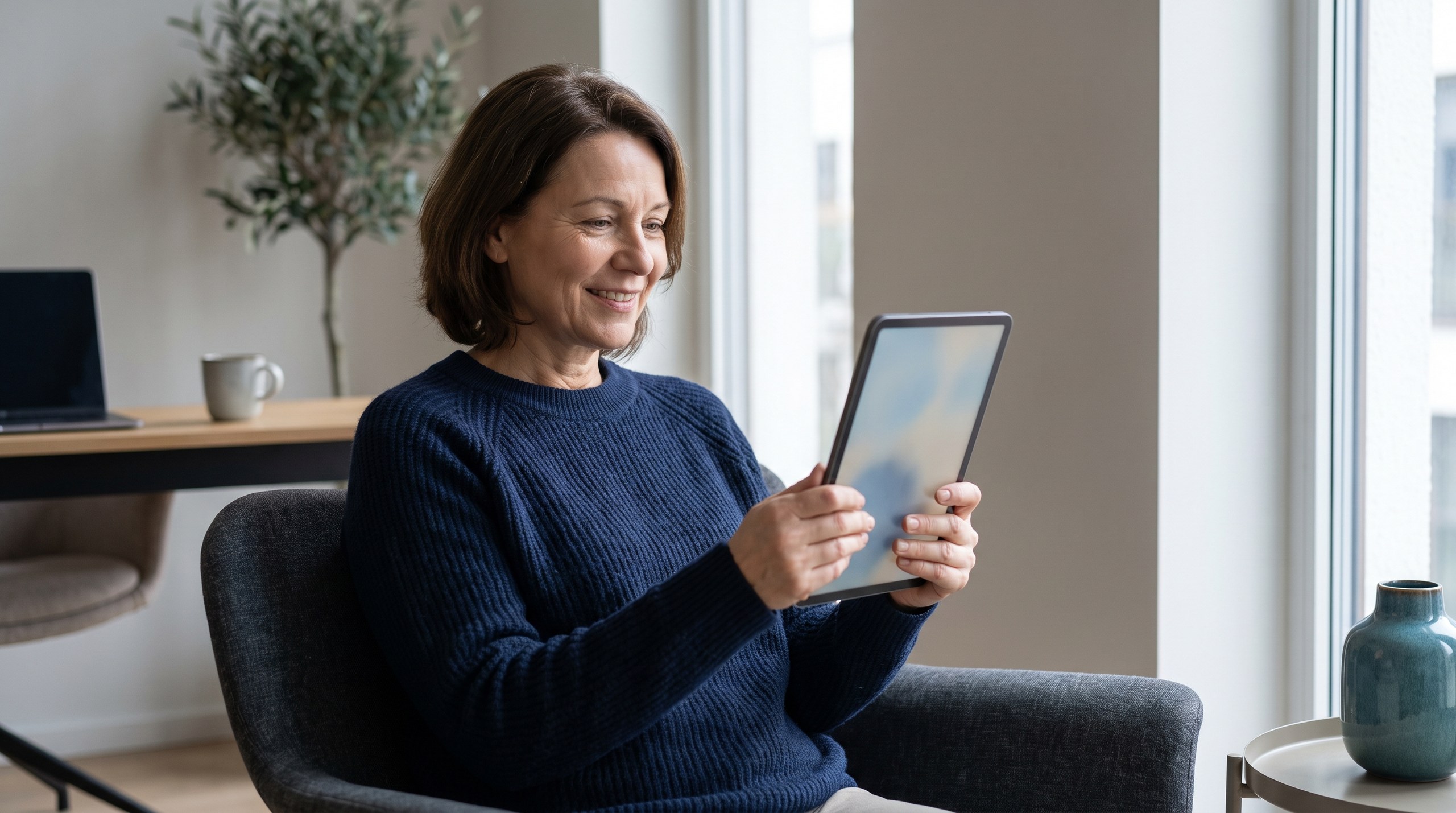 Frau sitzt entspannt im Sessel und verfolgt auf dem Tablet die Entwicklung ihres Tagesgelds